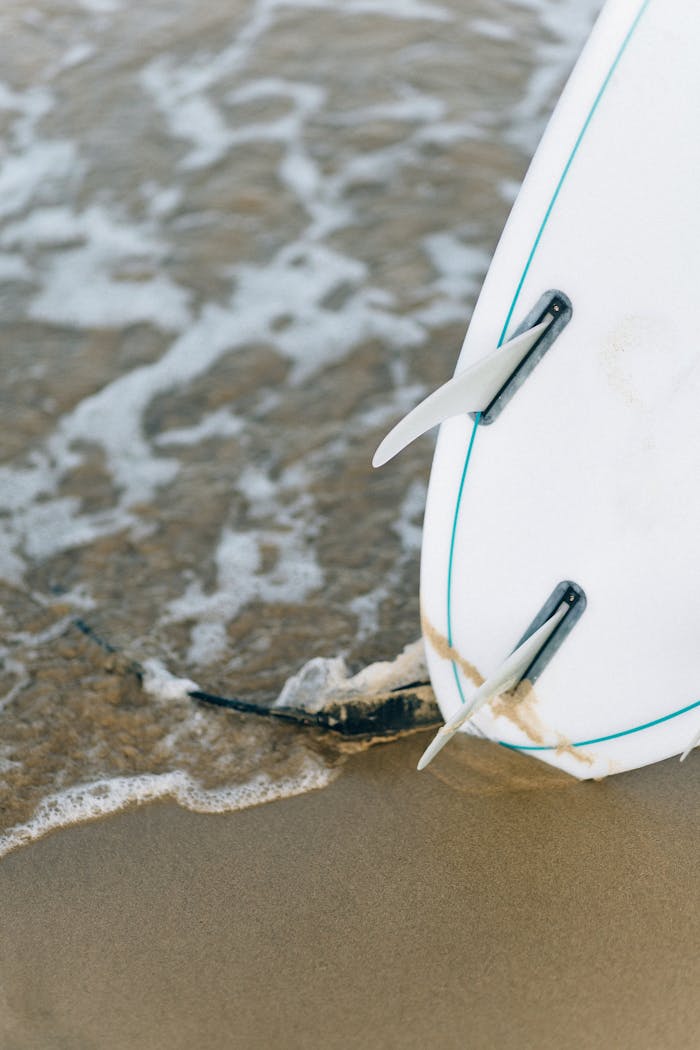 A detailed view of a surfboard resting on the wet sand with ocean waves.