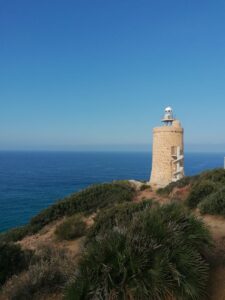 Camarinal Lighthouse on a cliff with ocean view and blue sky, perfect for travel inspiration.