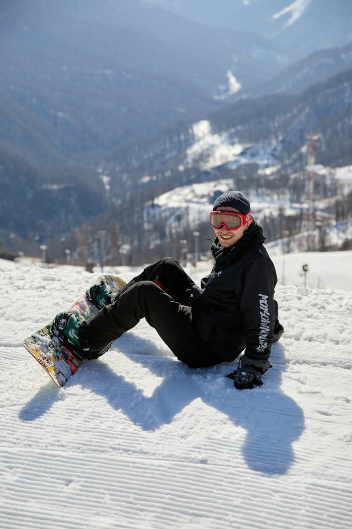Snowboarder taking a break on a sunny winter day with mountains in the background.