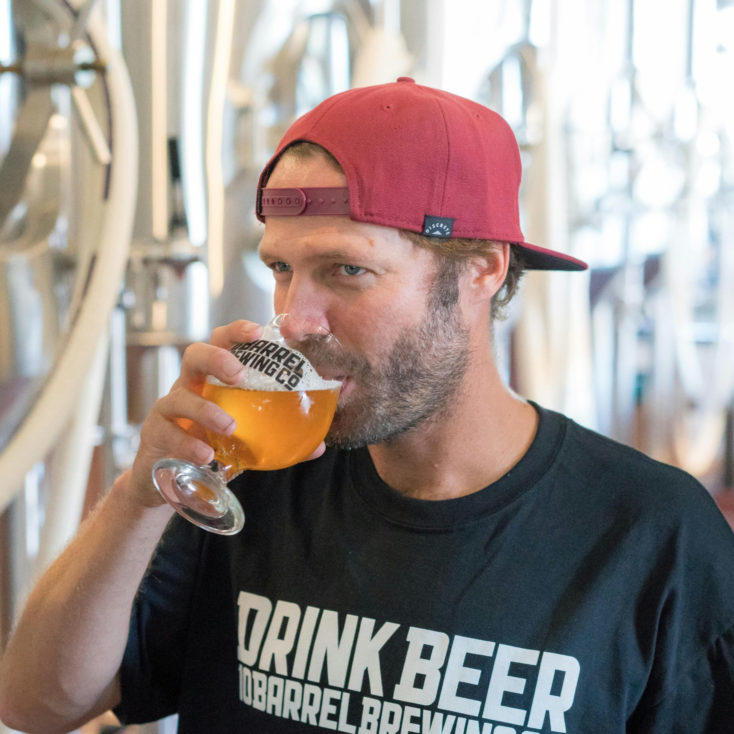 A man with a beard enjoys a glass of craft beer in a modern brewery environment.